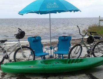 kayak, beach chairs, umbrella, and bikes set up on the beach