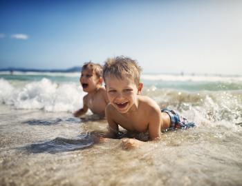 two little boys laying in the breaking waves on the beach